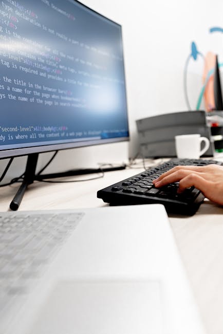 A close-up photograph of a computer screen displaying lines of HTML and CSS code in various colors, including red, green, purple, and blue, set against a black background. The code appears to be part